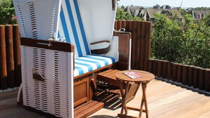 Un fauteuil de jardin en osier avec un coussin à rayures, une petite table en bois et une vue sur un quartier résidentiel.