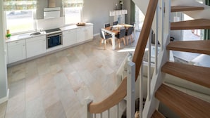 A modern kitchen with white cabinets, a dining area with a table and chairs, and a wooden staircase. - Holiday Home Sund-idyll (Kramerhof)