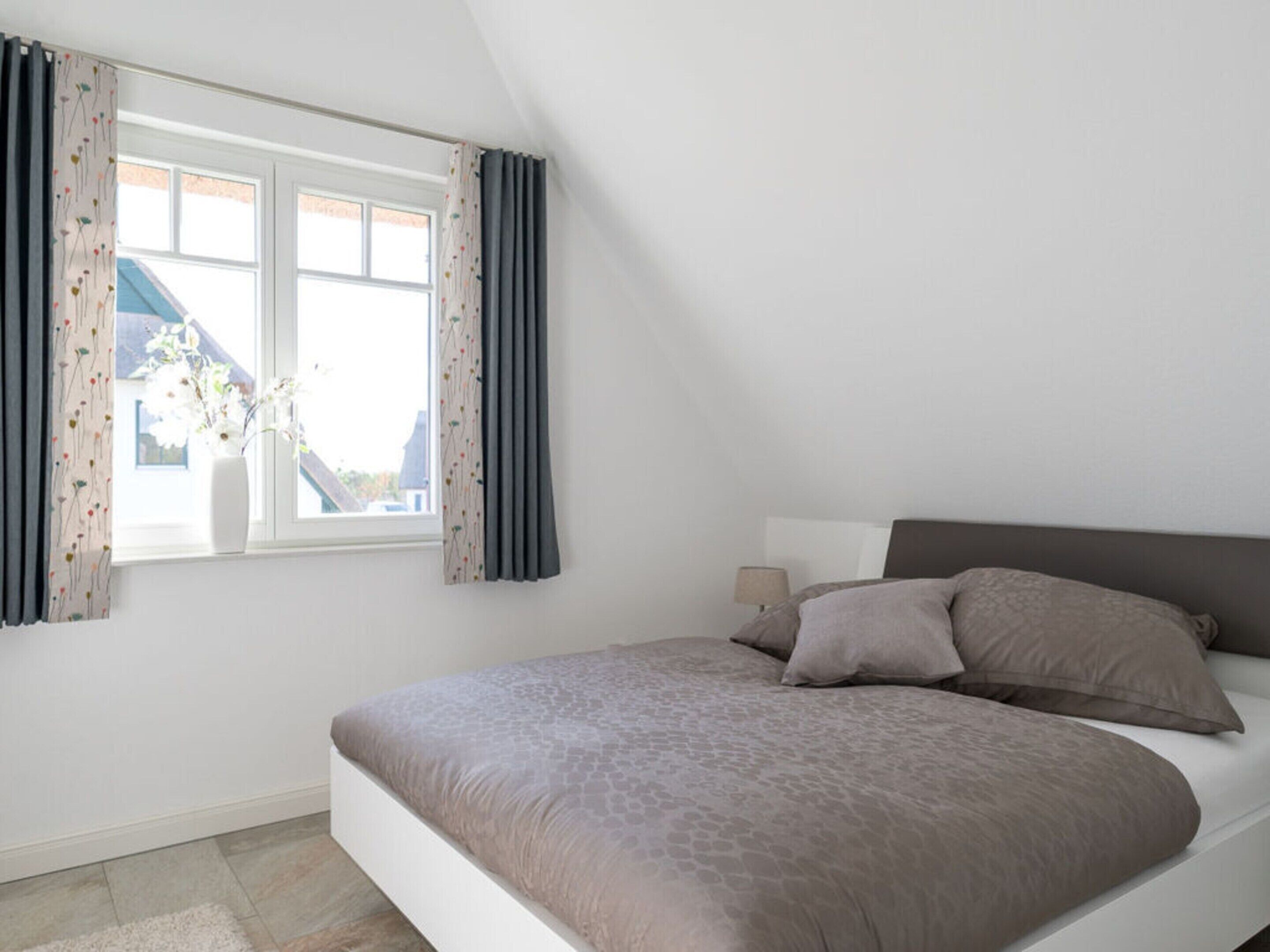 Een slaapkamer met een bed, een raam met gordijnen en uitzicht op een gebouw.
