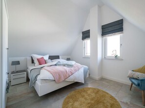 A bedroom with a bed, bedside tables, a chair, and a window with curtains. - Holiday Home Sund-idyll (Kramerhof)