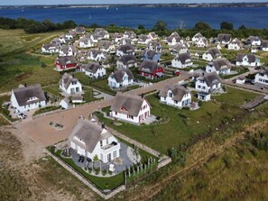 Une vue aérienne d’un village côtier aux maisons blanches, dont certaines sont rehaussées de touches de rouge, disposées selon un plan en forme de grille, offrant une vue dégagée sur la mer et les bateaux qui se trouvent au loin.