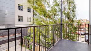 Un balcone con ringhiera in metallo che si affaccia su una strada e degli alberi.