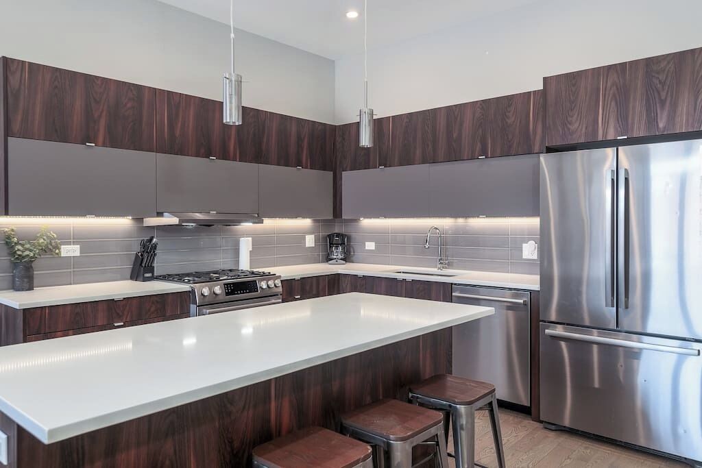 A modern kitchen with dark wood cabinets, stainless steel appliances, a large island, and bar stools.