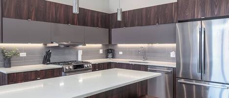 A modern kitchen with dark wood cabinets, stainless steel appliances, a large island, and bar stools.