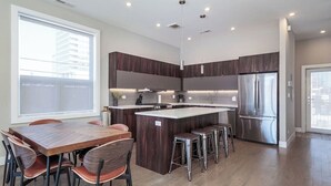 Een moderne keuken met een centraal eiland, donker houten kasten, roestvrijstalen apparatuur en een groot raam dat natuurlijk licht binnenlaat.