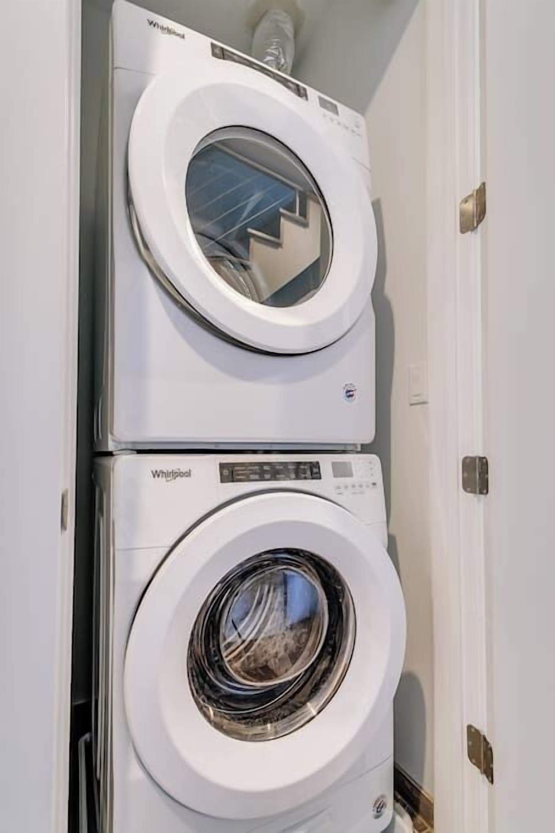 Une machine à laver et un sèche-linge Whirlpool superposés, dans une pièce aux murs blancs et dotée d’une porte.