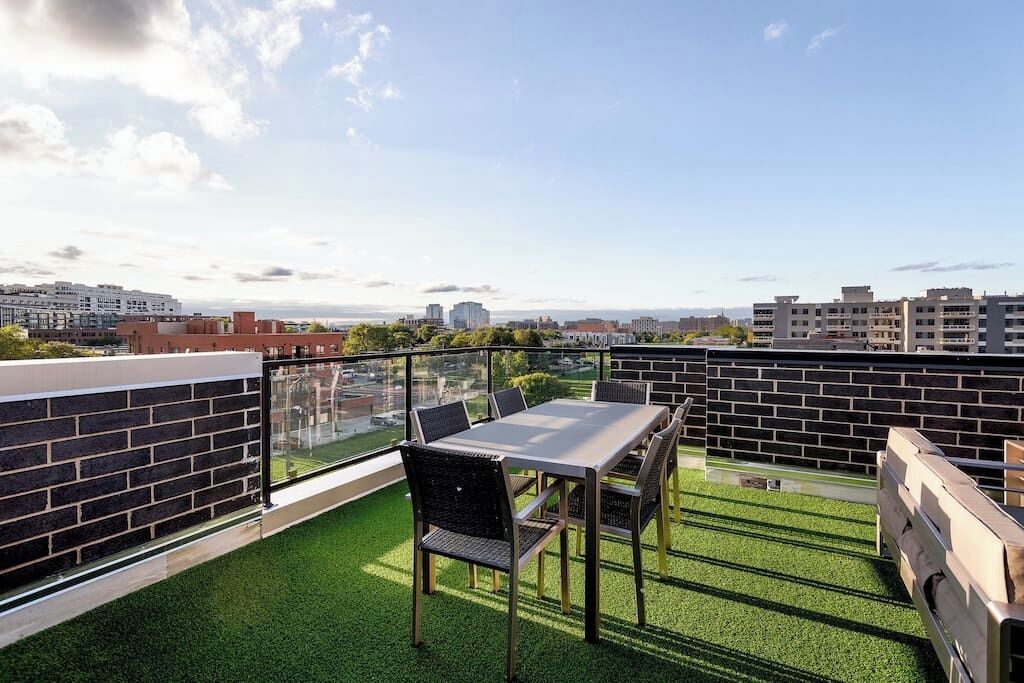 A rooftop terrace with a table and chairs, a glass balustrade, and a view of the cityscape.