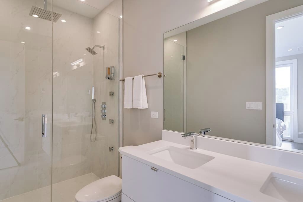 A modern bathroom with a glass-enclosed shower, a white sink, and a large mirror.