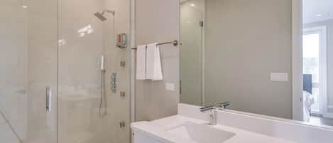 A modern bathroom with a glass-enclosed shower, a white sink, and a large mirror.