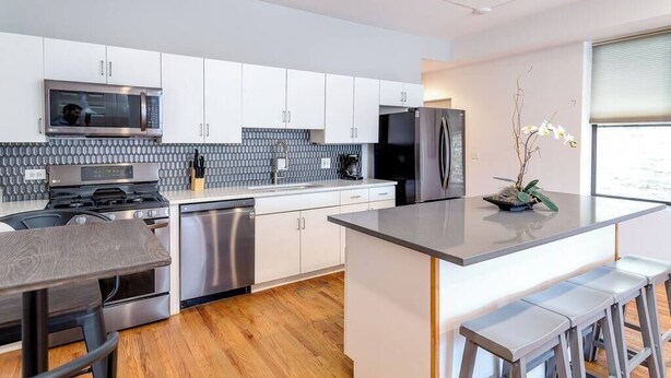 A modern kitchen with white cabinets, stainless steel appliances, a wooden table, and a bar area. - Downtown Goose Island with access to patio - 1 (Chicago)