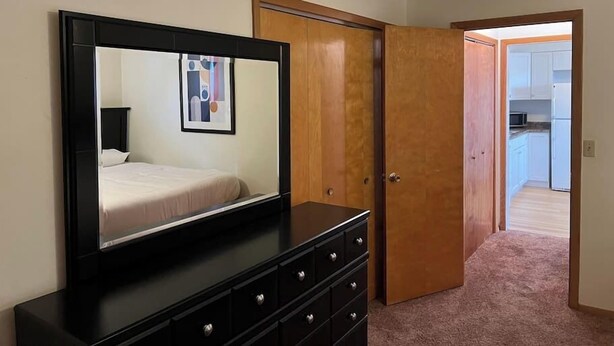 A bedroom with a large mirror, a bed, a dresser, and a door leading to a kitchen. - Close to Downtown - 2 queen beds (Springfield)