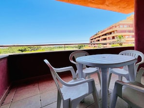 A balcony with a round table and four chairs, overlooking a building and greenery. - Belvilla by OYO Pelacanos Beach (Roquetas de Mar)