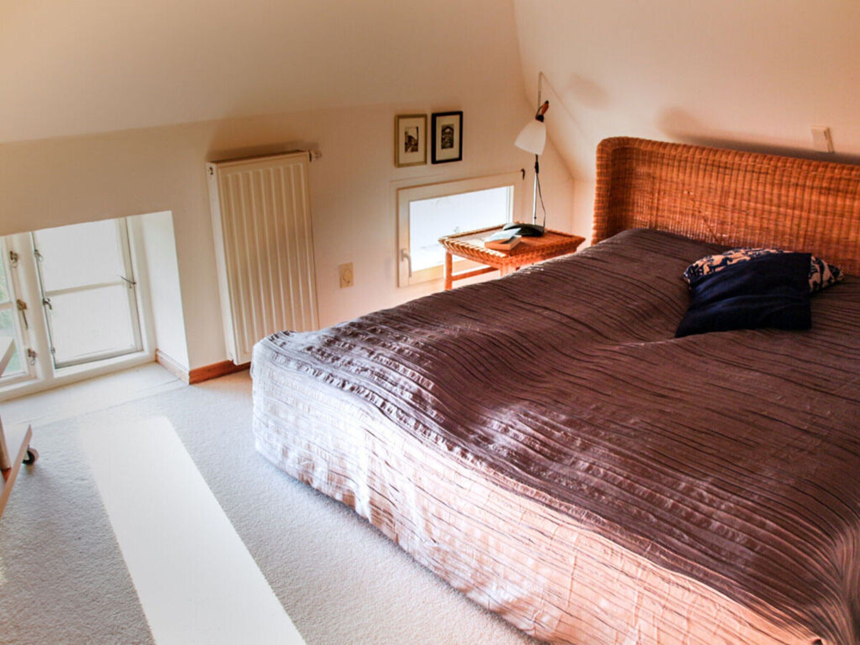 Ein Schlafzimmer mit einem großen Bett, einem Fenster, einem Heizkörper, einer Lampe und einem kleinen Tisch.