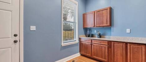 A kitchen with blue walls, wooden cabinets, a window with blinds, and a white door.