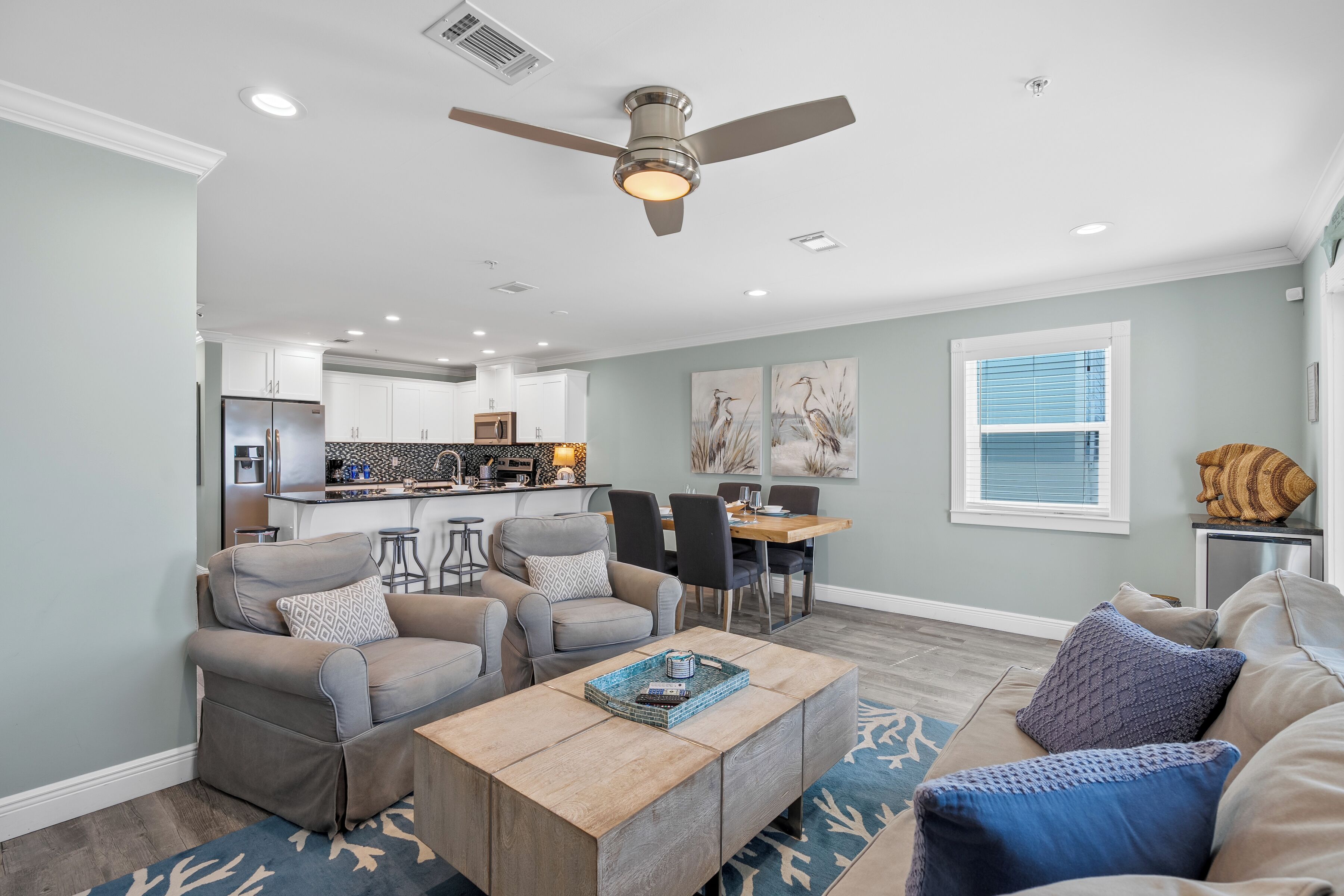 A spacious living room with a dining area, a kitchen in the background, and a ceiling fan.