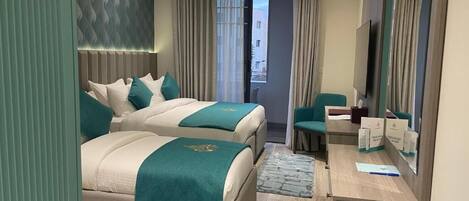 A modern hotel room with two beds, a desk, a chair, and a large mirror.