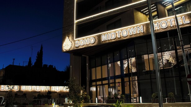 The exterior of Soho Midtown Hotel with illuminated signage and large windows. - Soho Midtown Hotel (Amman)