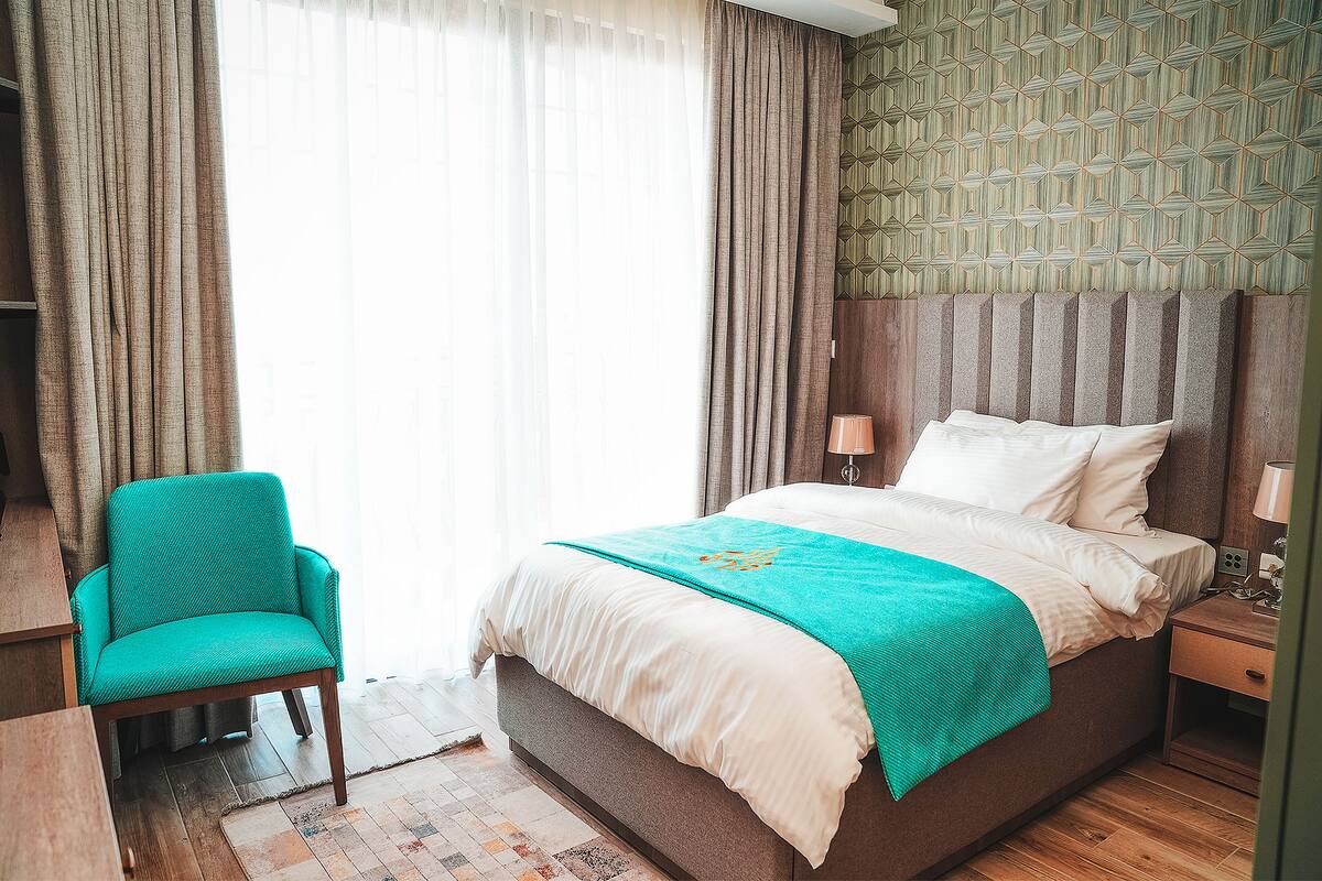 A bedroom with a bed, a chair, a nightstand, and a window with curtains.