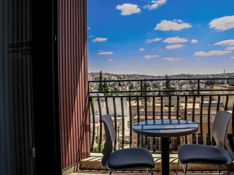 Un balcón con una mesa y dos sillas, con vista a un paisaje urbano con edificios y cielo despejado.