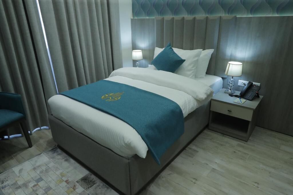 A hotel room with a bed, a nightstand, a chair, and a curtain.