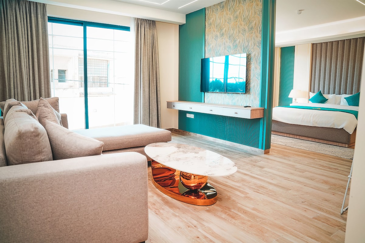 A modern hotel room with a sofa, a marble coffee table, a bed, and a TV mounted on the wall.