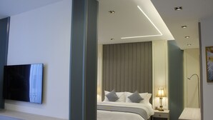 A modern hotel room with a large bed, bedside table, lamp, and a flat-screen TV mounted on the wall. - Soho Midtown Hotel (Amman)