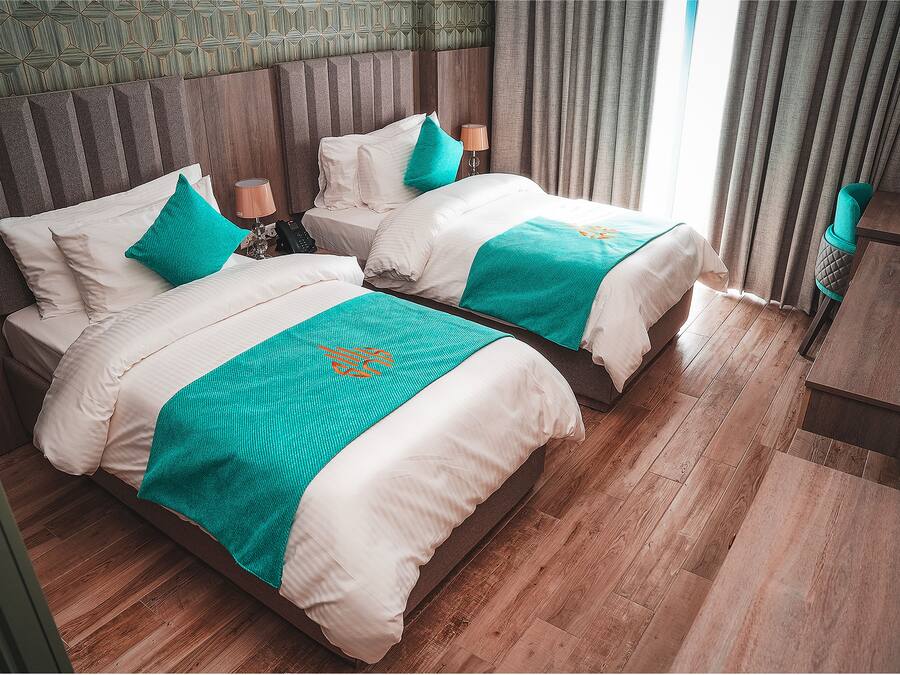 Ein Hotelzimmer mit zwei Betten, Holzboden, einem gemusterten Wandbild und Blick ins Freie.
