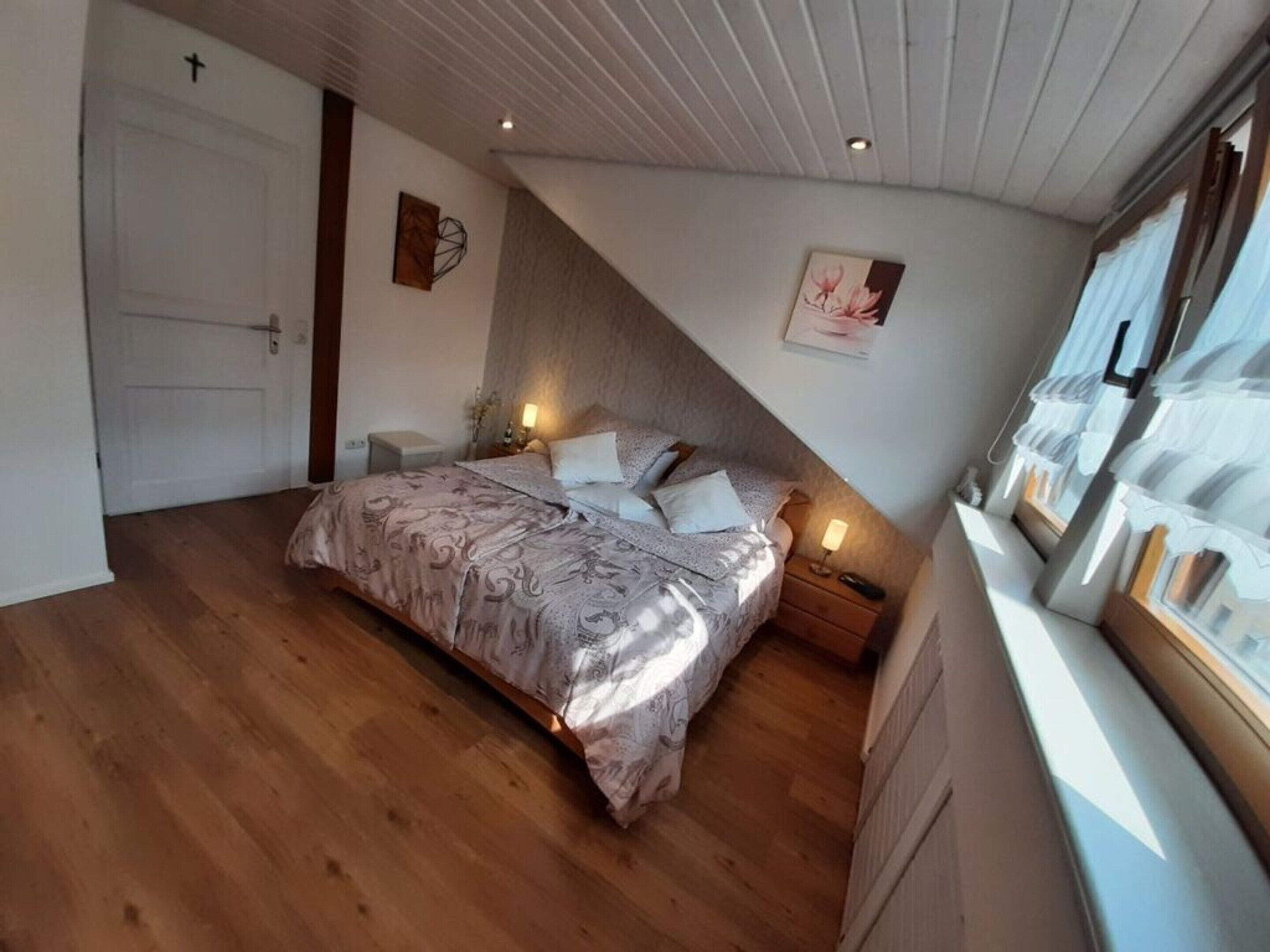 Ein Schlafzimmer mit einem Bett, Nachttischen, einem Fenster mit Vorhängen und einer Tür.