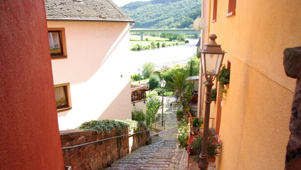 A narrow cobblestone street flanked by buildings with a river and bridge in the background. - Holiday Apartment Magnolia (Ockfen)