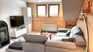 A modern living room with a sofa, a TV, a fireplace, and a dining area. - Holiday Apartment Magnolia (Ockfen)