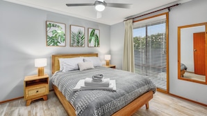 Un dormitorio con cama, mesitas de noche, ventilador de techo y ventana con persianas.