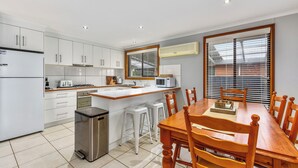 Una cocina moderna con armarios blancos, un refrigerador de acero inoxidable, un microondas y una mesa de comedor de madera con sillas.