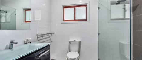 Un bany modern amb plat de dutxa de vidre, vàter blanc i pica de vidre.