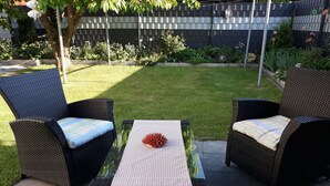 An outdoor seating area with two wicker chairs and a glass-top table, surrounded by a well-maintained lawn and a metal fence. - Also a Modern Retreat (Röbel/Müritz)
