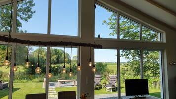 A spacious room with large windows, a dining table, and hanging light fixtures.