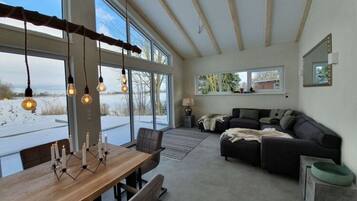A spacious living area with a large window, a wooden dining table, and a dark-colored sofa.