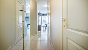 Un couloir avec des portes blanches, une cloison vitrée et une vue sur un espace de vie comprenant un canapé et une table.