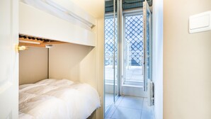 Une petite pièce compacte avec un lit superposé, une porte coulissante donnant sur un balcon et un aménagement simple et épuré.