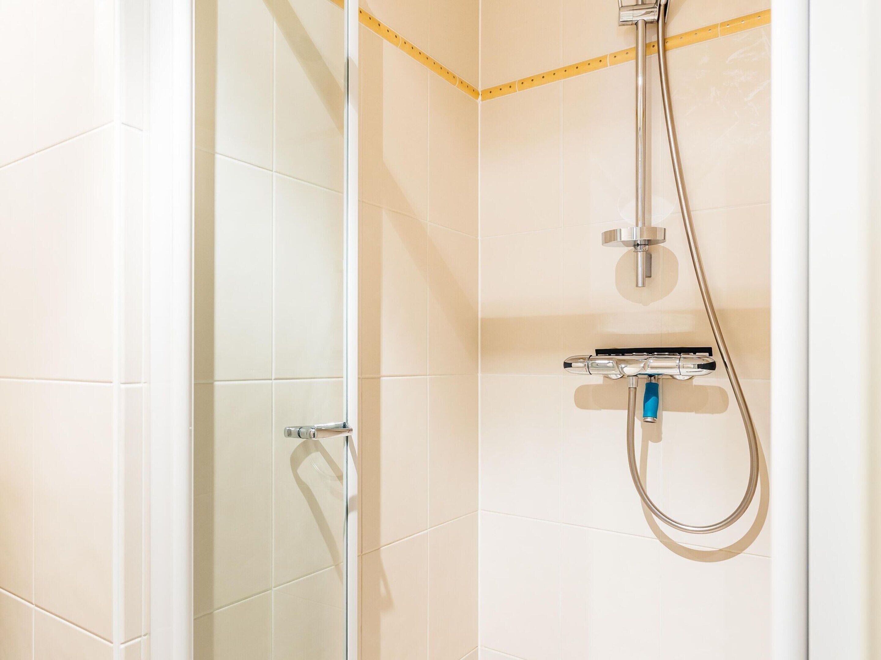 A shower with a handheld showerhead and a wall-mounted control panel.