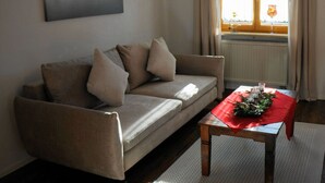 A living room with a sofa, a wooden coffee table, and a window with curtains. - Bader Modern Retreat (Blaichach)