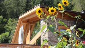 Una cabaña de madera con techo inclinado, rodeada de abundante vegetación y un paisaje boscoso.
