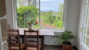 Habitación con un gran ventanal que ofrece vistas a un jardín y una masa de agua. Hay una mesa de madera con sillas y una planta en maceta en el alféizar.
