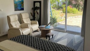 Una habitación moderna con dos sillones de cuero, un tapete estampado, una pequeña mesa redonda con un libro y un objeto decorativo, y un ventanal con vistas a un jardín y árboles rosados.