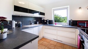A modern kitchen with white cabinets, a black countertop, and a window providing a view of greenery outside. - Maarchalet Modern Retreat (Daun)