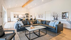 Een moderne woonkamer met een hoekbank, een salontafel en een keuken op de achtergrond.
