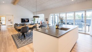 Een moderne keuken met een groot eiland, een eethoek met een houten tafel, en een woonkamer met een televisie en zitplaatsen.