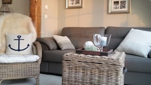 A cozy living room with a grey sofa, a wicker side table, and a fluffy chair with an anchor pillow.