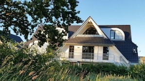 A two-story house with a sloped roof, a balcony with a railing, and a large window on the upper floor.