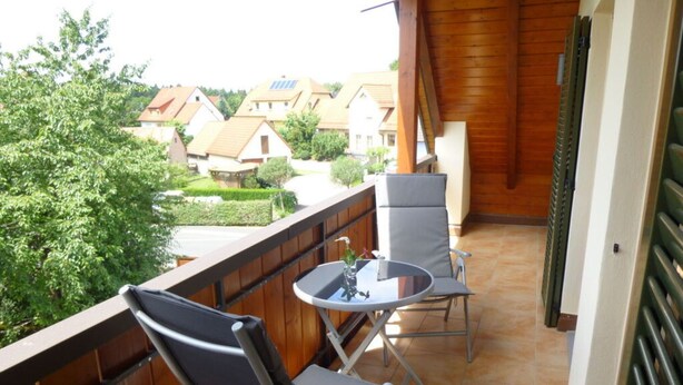A balcony with two chairs and a small table, overlooking a residential area with houses and greenery.