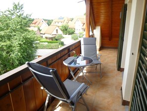 A balcony with two chairs and a small table, overlooking a residential area with houses and greenery. - Amazing Apartment in Gossweinstein (Goessweinstein)